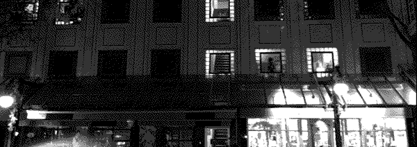 A three floor storefront lit up under night, only a few of its windows lit.