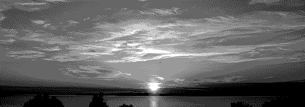 Clouds scattered around a placid sunset over a lake, mountains visible just over the horizon.